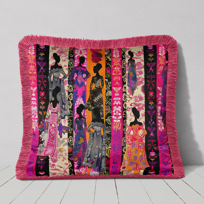 Decorative velvet luxury pillow in an eclectic bohemian style featuring silhouettes of women in vibrant, patterned dresses against vertical stripes in pink, orange, purple, and black. The pillow is bordered with a pink fringe.