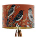 Intricately drawn birds, sit on branches and leaves with a rust orange backdrop on a classic sized 30x21cm handcrafted fabric lampshade by artist Kelly Stevens-McLaughlan