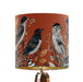 Intricately drawn birds, sit on branches and leaves with a rust orange backdrop on a small sized 20x18cm handcrafted fabric lampshade by artist Kelly Stevens-McLaughlan