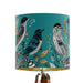 Intricately drawn birds, sit on branches and leaves with a blue backdrop on a small sized 20x18cm handcrafted fabric lampshade by artist Kelly Stevens-McLaughlan